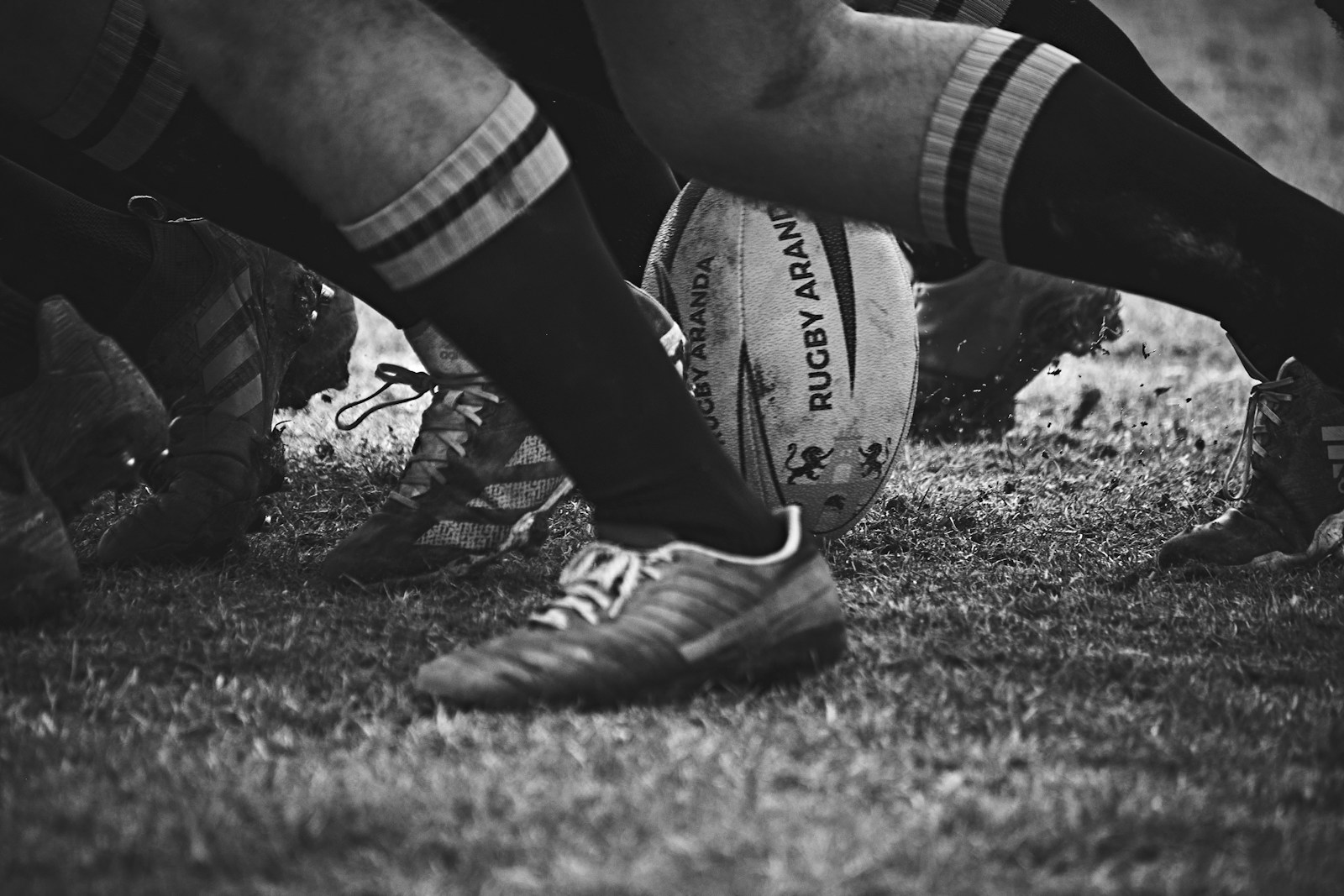 a close up of a rugby ball on the ground with only the player's feet visible on the grass