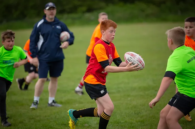 A young rugby player running with the ball and being watched by a Switch Rugby coach